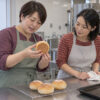 公民館の調理室で、焼いたパンの裏を同じサークルの女性に見せる49歳の真帆を描いたイメージ
