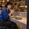 小さな洋食店のカウンターで、1人分の料理を選んで夕食を食べる50歳の佳乃を描いたイメージ