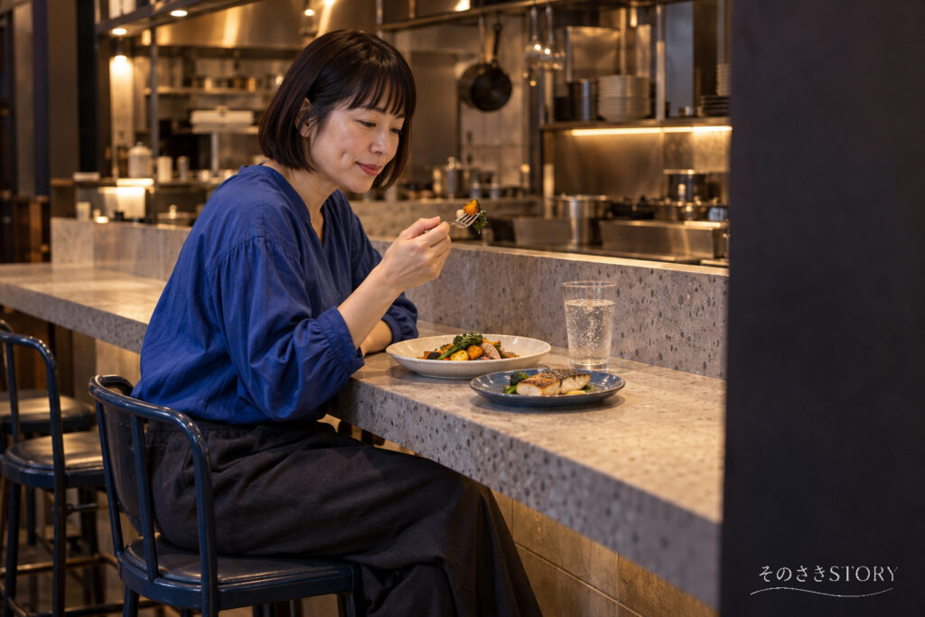 小さな洋食店のカウンターで、1人分の料理を選んで夕食を食べる50歳の佳乃を描いたイメージ