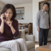 警察を名乗る電話を聞きながら、帰宅した夫に待ってと合図する女性