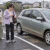 水が引いた駐車場で、水に浸かった愛車から離れ、鍵を鞄へしまう55歳の美津と24歳の娘を描いたイメージ