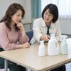 貸会議室で3本の洗剤を見ながら、友人の販売の説明を聞く52歳の女性のイメージ