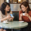 喫茶店で旅行の予算を話し合う56歳の恵里と友人の文香を描いたイメージ