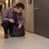 夜のマンション廊下で、鍵が見つからず鞄のポケットを探す54歳の圭吾のイメージ