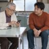 実家で自分のスマホを操作する78歳の耕造と、取り上げずに見守る50歳の息子・英嗣のイメージ