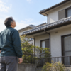 点検の訪問者を断った翌朝、自宅の庭から屋根を見上げる60歳の修司を描いたイメージ